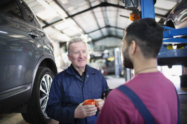 Männliche Mechaniker unterhalten sich und trinken Kaffee in einer Autowerkstatt - HOXF06413