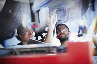 Männliche Mechaniker arbeiten unter einem Auto in einer Autowerkstatt - HOXF06415