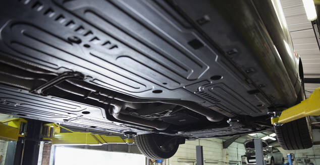 Undercarriage of car on hydraulic lift in auto repair shop - HOXF06419