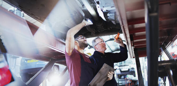 Männliche Mechaniker mit Taschenlampen arbeiten unter dem Auto in einer Autowerkstatt - HOXF06423