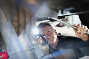 Männlicher Mechaniker mit Taschenlampe arbeitet unter dem Auto in einer Autowerkstatt - HOXF06425