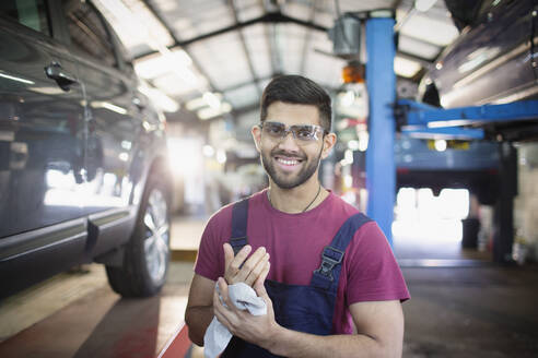 Porträt eines selbstbewussten männlichen Mechanikers, der sich in einer Autowerkstatt die Hände abwischt - HOXF06426