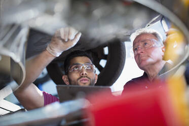 Männliche Mechaniker arbeiten unter einem Auto in einer Autowerkstatt - HOXF06427