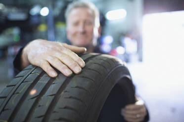 Männlicher Mechaniker hält Reifen in einer Autowerkstatt - HOXF06430