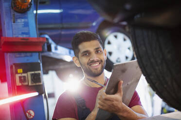 Porträt eines selbstbewussten, lächelnden männlichen Mechanikers mit Klemmbrett in einer Autowerkstatt - HOXF06431