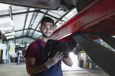 Porträt eines selbstbewussten männlichen Mechanikers mit Diagnosegeräten in einer Autowerkstatt - HOXF06435