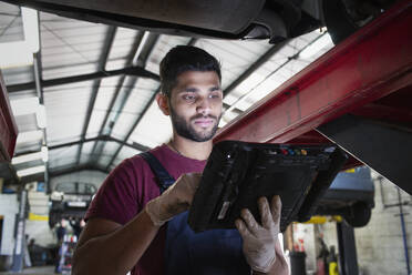 Fokussierter männlicher Mechaniker mit Diagnosegeräten in einer Autowerkstatt - HOXF06439