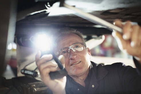 Männlicher Mechaniker mit Taschenlampe arbeitet unter dem Auto in einer Autowerkstatt - HOXF06440
