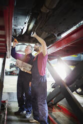 Männliche Mechaniker arbeiten unter einem Auto in einer Autowerkstatt - HOXF06446