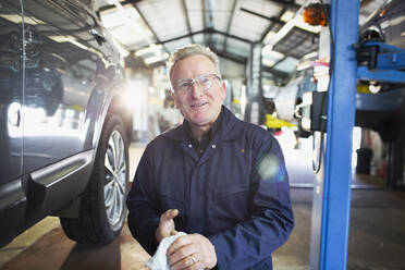 Portrait confident male mechanic wiping hands in auto repair shop - HOXF06447