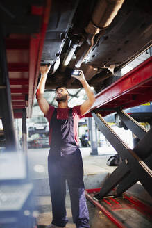 Männlicher Mechaniker arbeitet unter einem Auto in einer Autowerkstatt - HOXF06451