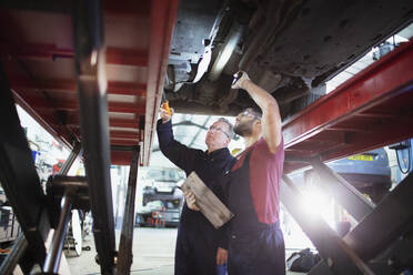 Männliche Mechaniker mit Taschenlampe arbeiten unter dem Auto in einer Autowerkstatt - HOXF06453