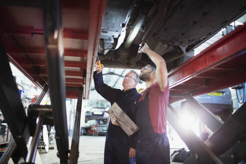 Männliche Mechaniker mit Taschenlampe arbeiten unter dem Auto in einer Autowerkstatt - HOXF06453