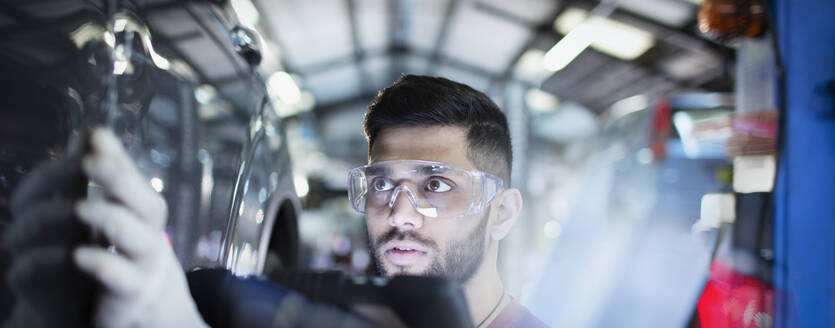Fokussierter männlicher Mechaniker, der ein Auto in einer Autowerkstatt untersucht - HOXF06465