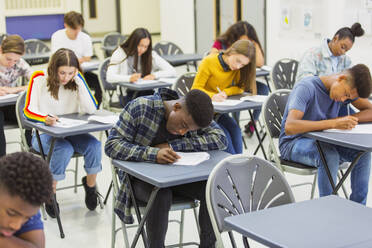 Fokussierte Oberstufenschüler, die an den Tischen im Klassenzimmer eine Prüfung ablegen - CAIF27968