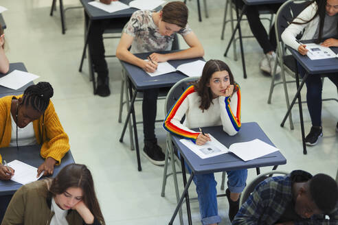 Nachdenkliches High-School-Mädchen, das eine Prüfung am Schreibtisch im Klassenzimmer ablegt - CAIF27972