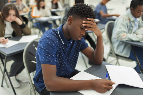 Konzentrierter High-School-Junge, der eine Prüfung am Schreibtisch im Klassenzimmer ablegt - CAIF27975