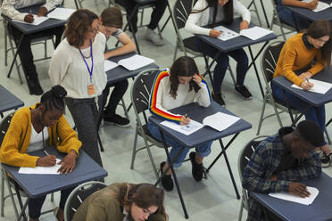 Gymnasiallehrer beaufsichtigt Schüler, die an Tischen Prüfungen ablegen - CAIF27979