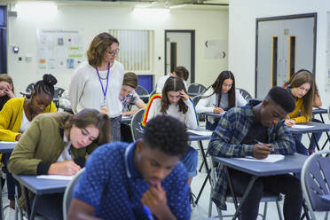 Gymnasiallehrer beaufsichtigt Schüler, die an den Pulten Prüfungen ablegen - CAIF27982