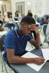 Konzentrierter Schüler, der am Schreibtisch im Klassenzimmer eine Prüfung ablegt - CAIF27987