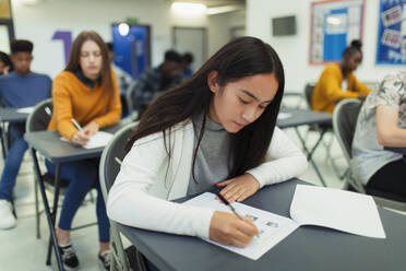 Konzentrierte Schülerin, die am Schreibtisch im Klassenzimmer eine Prüfung ablegt - CAIF27989