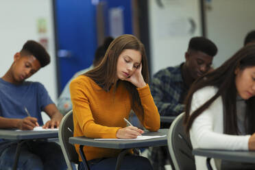 Konzentrierte Schülerin, die am Schreibtisch im Klassenzimmer eine Prüfung ablegt - CAIF27995
