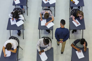 Gymnasiallehrer beaufsichtigt Schüler, die an den Pulten Prüfungen ablegen - CAIF27996