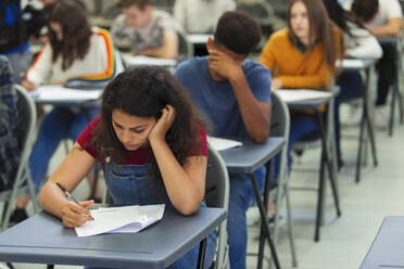 Konzentrierte Schülerin, die am Schreibtisch im Klassenzimmer eine Prüfung ablegt - CAIF27997