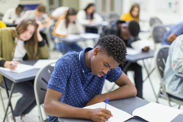 Focused high school boy student taking exam at desk in classroom - CAIF27999