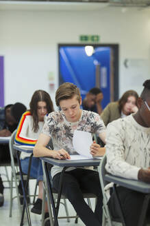 Konzentrierter Schüler, der am Schreibtisch im Klassenzimmer eine Prüfung ablegt - CAIF28012