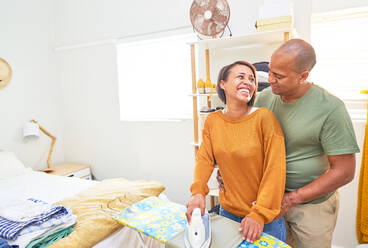 Happy couple ironing and talking in bedroom - CAIF28025