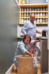 Happy couple doing laundry in kitchen - CAIF28083