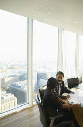 Business people discussing paperwork in highrise conference room meeting - CAIF28125