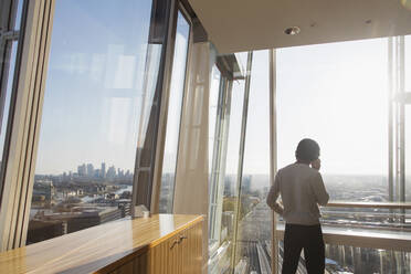 Businessman talking on smart phone at sunny modern highrise window - CAIF28129