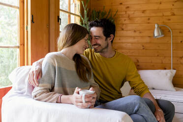 Smiling couple romancing while sitting on sofa in log cabin - LVVF00005