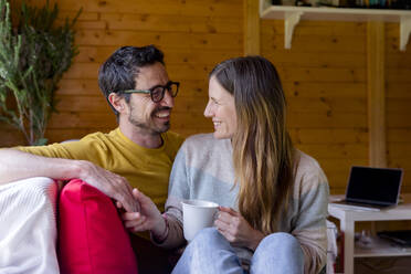 Romantic couple looking at each other while relaxing on sofa in log cabin - LVVF00008