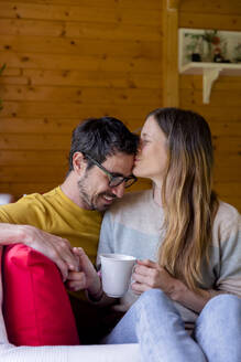 Liebende Frau küsst Mann auf die Stirn, während sie sich in einer Blockhütte entspannt - LVVF00009