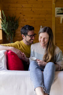 Fröhliches Paar hält sich an den Händen und entspannt sich auf dem Sofa in einer Blockhütte - LVVF00012