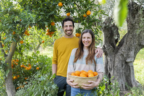 Lächelndes Paar mit Orangen an Bäumen auf einem Bio-Bauernhof - LVVF00035