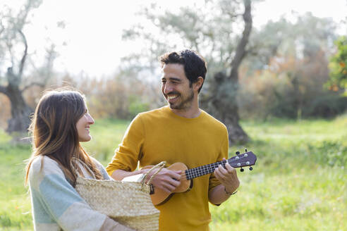 Frau, die einen Weidenkorb trägt, während ein glücklicher Mann auf dem Lande Gitarre spielt - LVVF00041