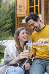 Happy man pouring wine in glass held by girlfriend while sitting outdoors - LVVF00055
