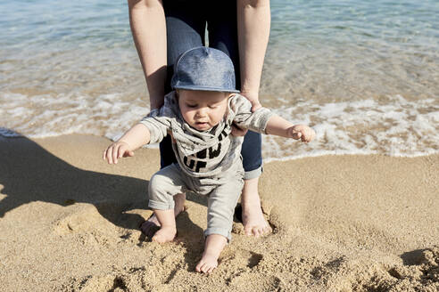 Tiefschnitt einer Mutter, die ihrem Sohn beim Gehen am Sandstrand hilft - JNDF00162