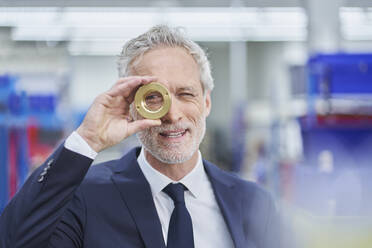 Confident male manager looking through brass object in factory - RORF02158