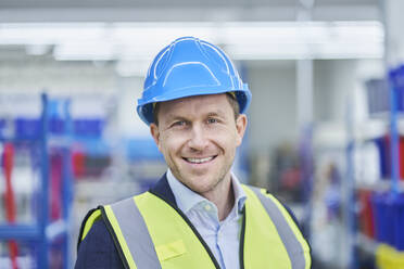 Happy male supervisor wearing hardhat and reflective clothing in factory - RORF02160