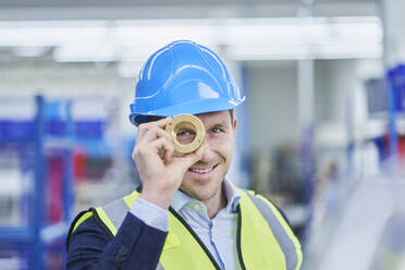 Happy male supervisor looking through brass object in factory - RORF02162