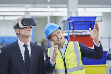 Ein männlicher Vorgesetzter erklärt einem Manager, der eine VR-Brille trägt, seinen Plan in einer Fabrik - RORF02163