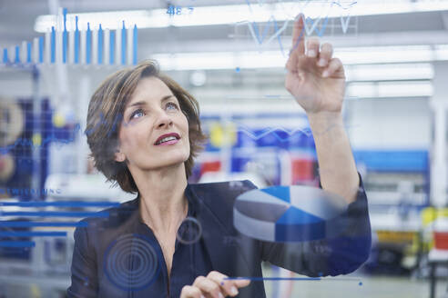 Weibliche Managerin berührt Liniendiagramm auf Glas in der Industrie - RORF02182