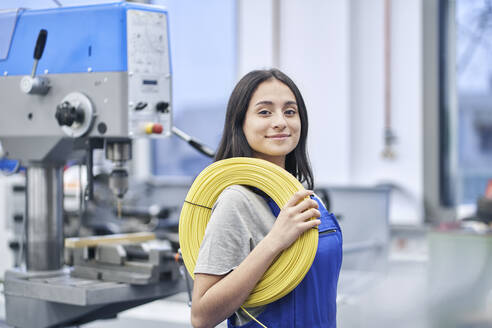 Glückliche Arbeiterin trägt aufgerollte Kabel in einer Fabrik - RORF02220