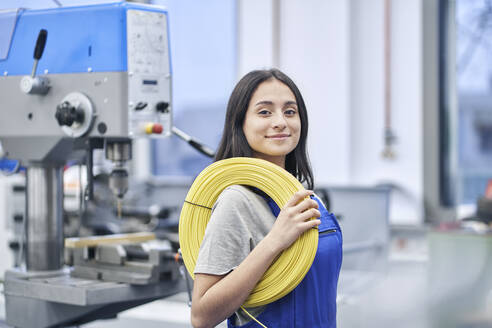 Happy female worker carrying rolled up cables in factory - RORF02220