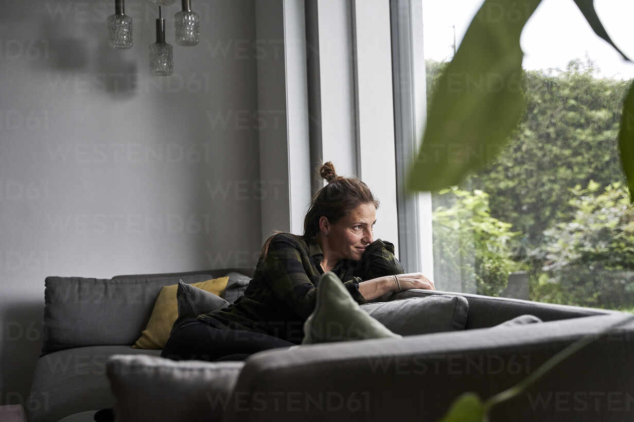 Distracted lady looking outside through a window sitting on a couch in the  living room at home Stock Photo - Alamy